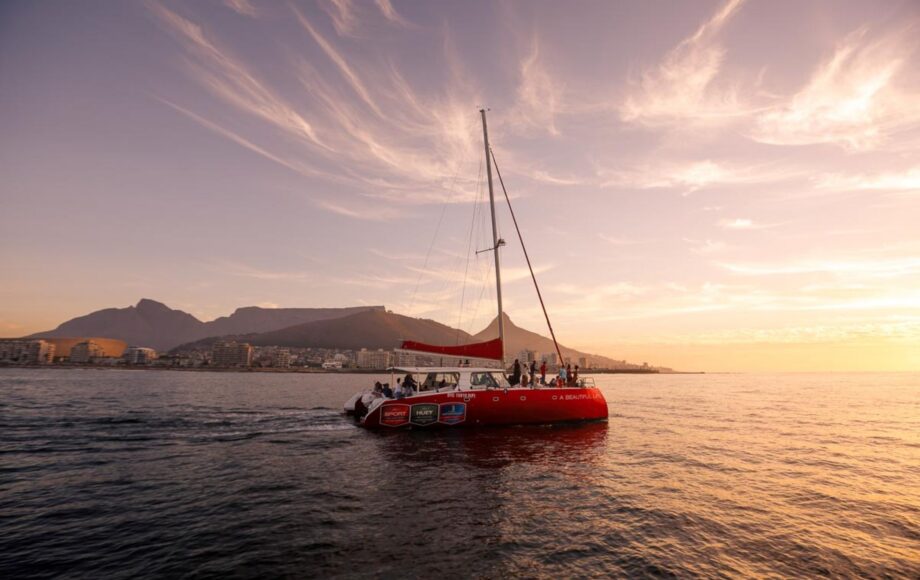 Velero frente a una costa montañosa con la puesta de sol