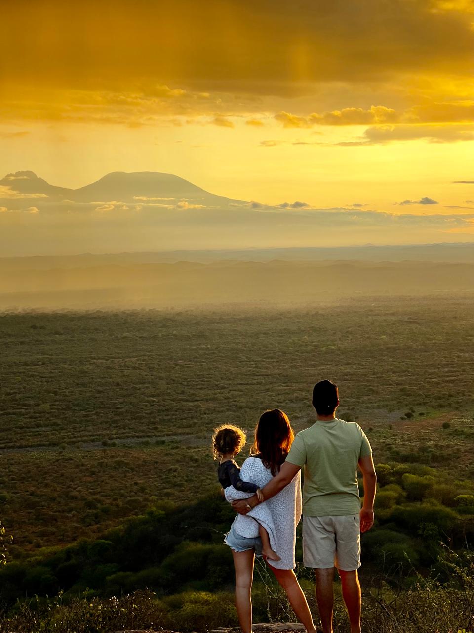 Familia con un niño pequeño en brazos contemplando la puesta de sol.