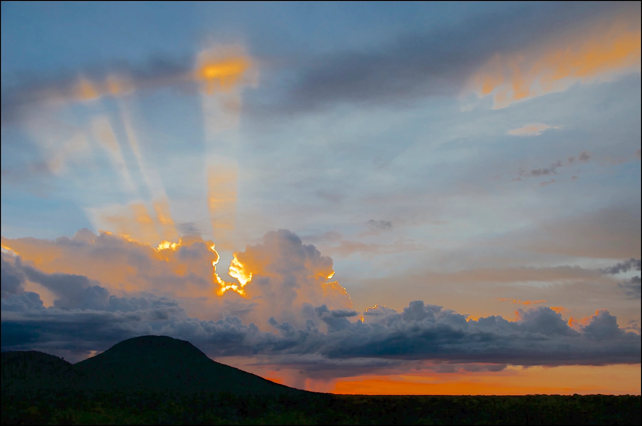Nubes oscuras sobre la Reserva Natural de Okonjima, Namibia, con montañas en primer plano y el sol asomando entre las nubes